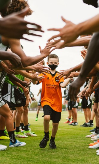 Boy wearing MDAnderson soccer uniform running through a tunnel of people giving high fives.